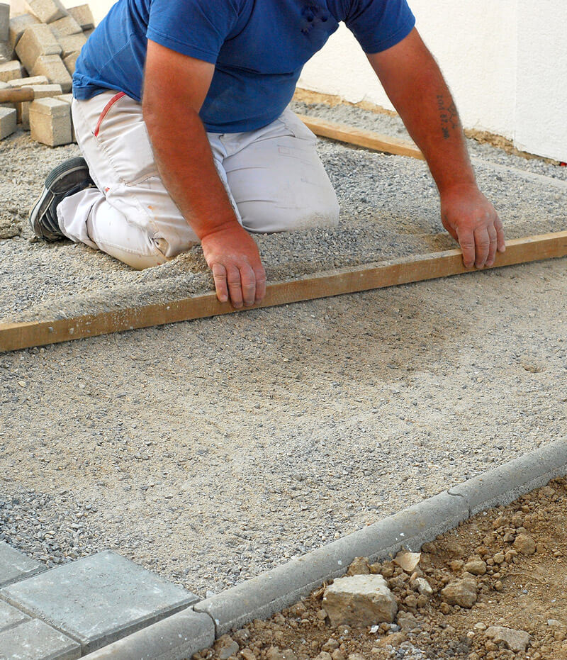 Landscape worker leveling brick paver limestone base