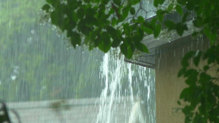 A heavy rain storm with an overflowing gutter on the corner of a house.