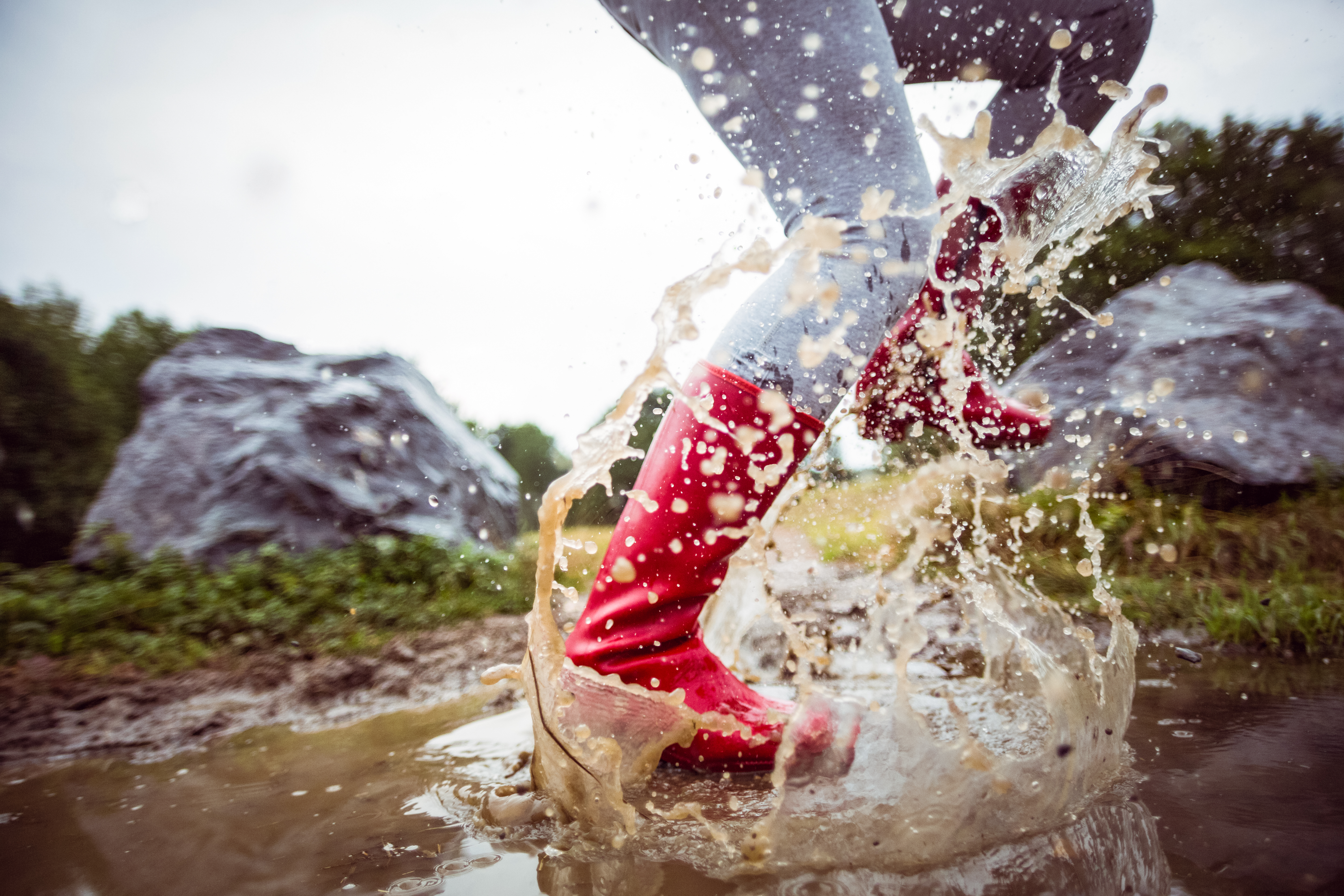 A woman wearing rain boots splashing through a puddle in the yard.