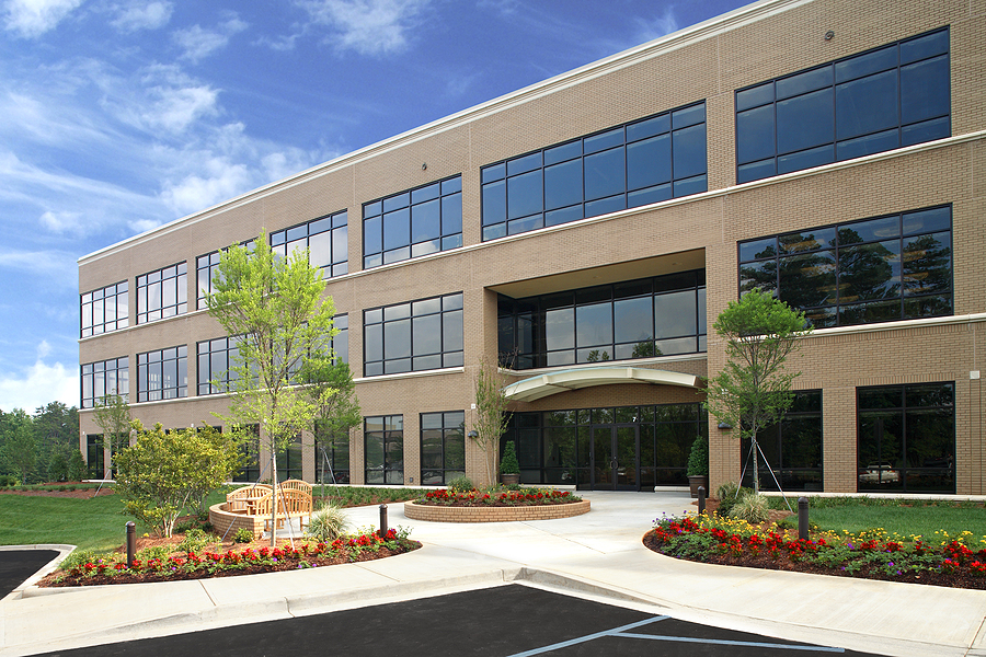 Brick office building exterior with lush landscaping with trees and flowers.