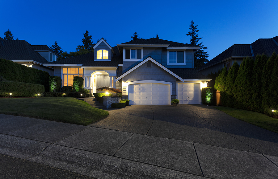 Modern suburban home exterior on a late summer evening with outdoor lights on yard and house.