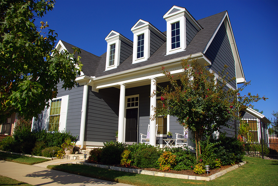 Idealistic Victorian style two story house with three large windows well manicured front yard with green grass shrubs and flowers.