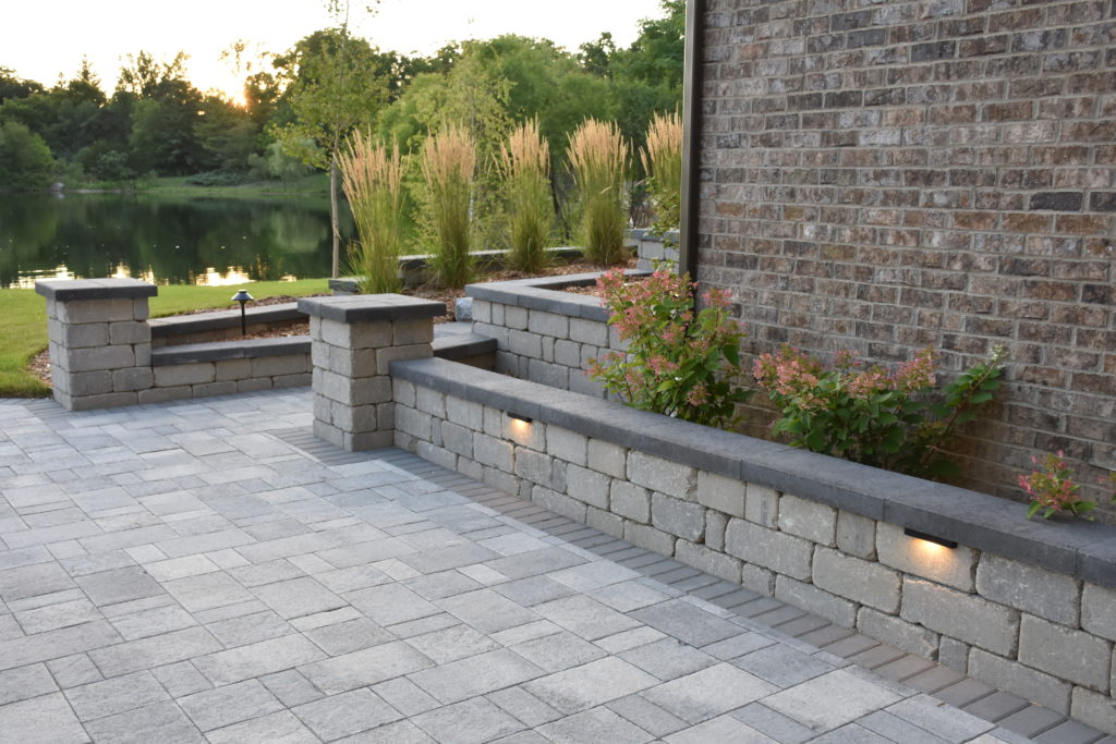 Brick retaining wall with flower bed behind it and accent lights.