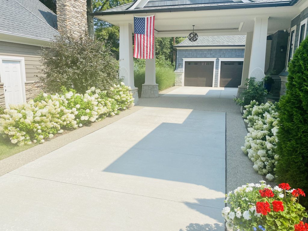 Beautiful newly poured cement driveway with a car port lined with perennials.