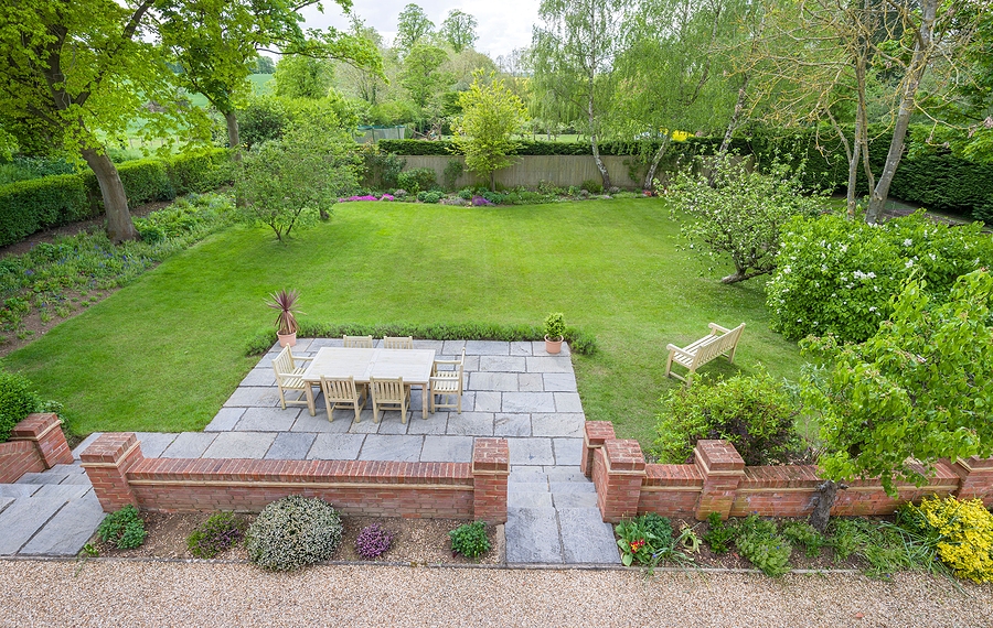 Back yard with green grass, retaining brick wall, paver patio, and patio furniture.