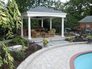 Patio surrounding an inground pool a small raised gazebo had patio furnature dining set under it adjecent to the paved patio pool area