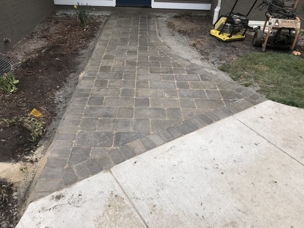 Walkway with brown brick pavers connecting to concrete